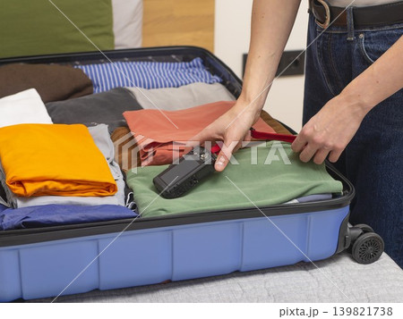 Open suitcase with clothes and camera on bed during packing. Indoor travel preparation scene showing 139821738