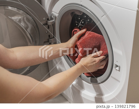 Hand putting dirty towel, loading textile, placing cloth into home washer, washing machine appliance. Hand putting dirty towel, loading textile, placing cloth into home washer, washing machine appliance. 139821796