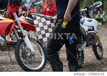 Candid moment of a racing official with a checkered flag in a busy paddock. Candid moment of a racing official with a checkered flag in a busy paddock. 139823110