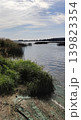 Polluted natural landscape with stagnant green river water and muddy shoreline. Atmospheric composition highlights environmental damage. 139823354