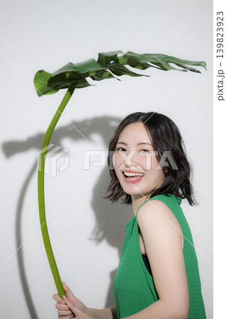 モンステラの葉を傘にするかわいい笑顔の日本人女性、傘や夏の自然のイメージカメラ目線の上半身 モンステラの葉を傘にするかわいい笑顔の日本人女性、傘や夏の自然のイメージカメラ目線の上半身 139823923