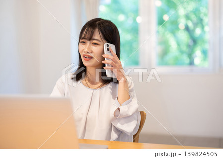 パソコンで作業しながらスマートフォンで通話する日本人の若い女性 139824505