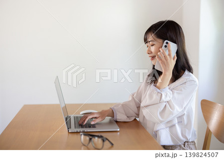 パソコンで作業しながらスマートフォンで通話する日本人の若い女性 パソコンで作業しながらスマートフォンで通話する日本人の若い女性 139824507