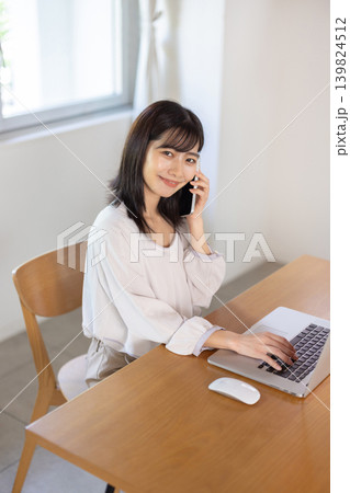 パソコンで作業しながらスマートフォンで通話する日本人の若い女性 139824512