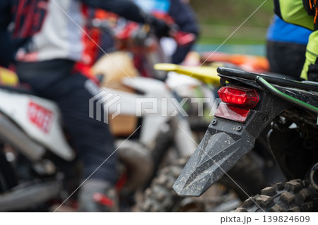 Intense pre-race atmosphere with a glowing brake light and blurred riders. Red tail light of an enduro motorcycle in a paddock. 139824609
