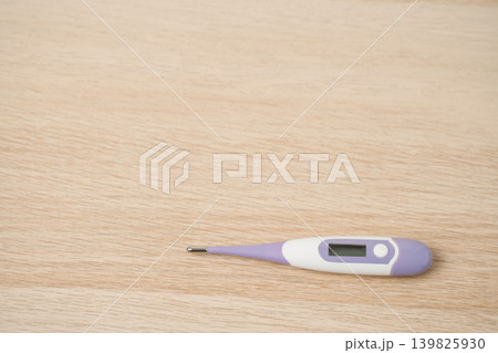 Purple and white digital thermometer lying on a light wooden table, used for measuring body temperature, fever monitoring and home health care. Simple health, illness and personal care concepts. Purple and white digital thermometer lying on a light wooden table, used for measuring body temperature, fever monitoring and home health care. Simple health, illness and personal care concepts. 139825930