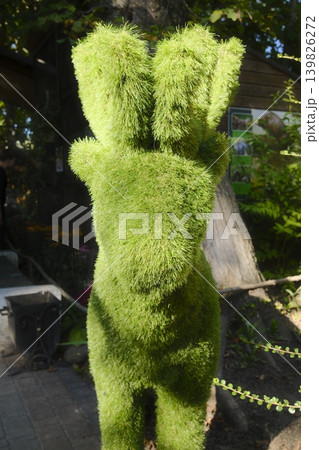 A green topiary in the shape of a woman stands in a park setting A green topiary in the shape of a woman stands in a park setting 139826272