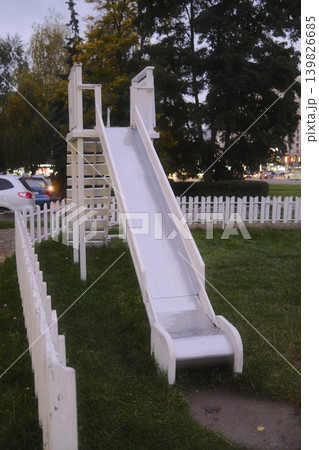 A slide is visible in a playground surrounded by a white fence. It is evening 139826685