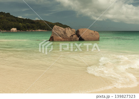 Tropical beach features granite boulders in calm turquoise Ocean and white sand Tropical beach features granite boulders in calm turquoise Ocean and white sand 139827323