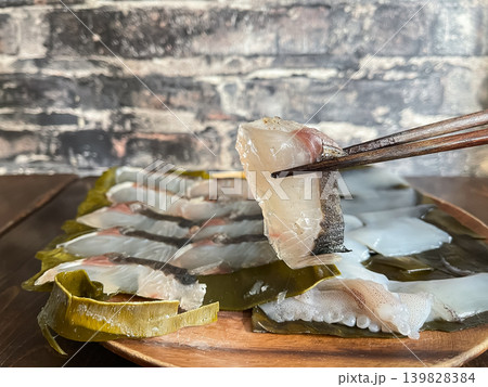 サワラとアオリイカの昆布締め。新鮮な刺身を昆布で包んで熟成させた料理。サワラを箸あげしているところ。 139828384