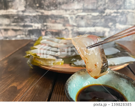 サワラとアオリイカの昆布締め。新鮮な刺身を昆布で包んで熟成させた料理。サワラを箸あげしているところ。 サワラとアオリイカの昆布締め。新鮮な刺身を昆布で包んで熟成させた料理。サワラを箸あげしているところ。 139828385