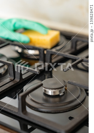 Cleaning a gas hob with a sponge and glove, removing grease in a modern kitchen. 139828471
