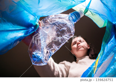 Woman throwing plastic bottle into blue trash bag. Low angle. Look from the inside of bag. High quality image Woman throwing plastic bottle into blue trash bag. Low angle. Look from the inside of bag. High quality image 139828751