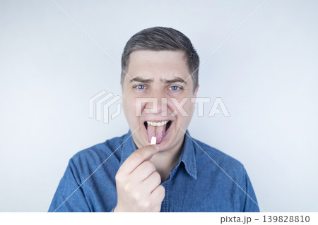 Man suffering from phagophobia struggling to swallow pill. Caucasian male looking anxious and scared before taking medication, experiencing fear of choking or swallowing difficulties. Man suffering from phagophobia struggling to swallow pill. Caucasian male looking anxious and scared before taking medication, experiencing fear of choking or swallowing difficulties. 139828810
