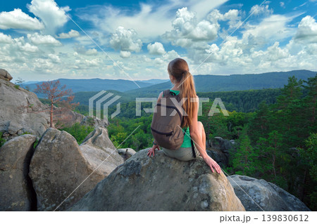 Tired hiker girl relaxing on rocky mountain top enjoying summer nature during travelling on wilderness trail. Lonely woman traveler traversing high hilltop route. Healthy lifestyle concept Tired hiker girl relaxing on rocky mountain top enjoying summer nature during travelling on wilderness trail. Lonely woman traveler traversing high hilltop route. Healthy lifestyle concept 139830612