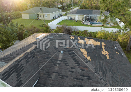 Damaged house roof with missing shingles after hurricane Ian in Florida. Consequences of natural disaster Damaged house roof with missing shingles after hurricane Ian in Florida. Consequences of natural disaster 139830649