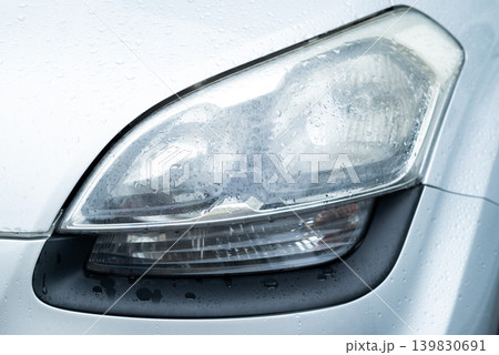 Close-up of a foggy car headlight covered in water droplets on a silver vehicle Close-up of a foggy car headlight covered in water droplets on a silver vehicle 139830691