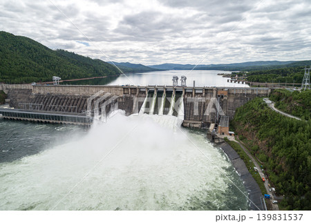 Aerial view of concrete dam releasing water into river on cloudy day. Water discharge at hydroelectric power plant. Aerial view of concrete dam releasing water into river on cloudy day. Water discharge at hydroelectric power plant. 139831537