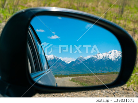 Distant snow-capped mountain peaks and a brilliant blue sky reflect in a vehicle's side mirror 139831573