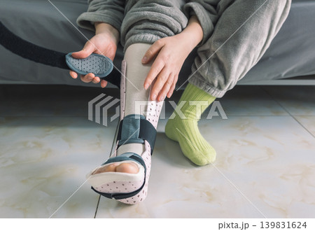 Hands adjust the strap on a patient's light pink perforated medical foot and ankle brace Hands adjust the strap on a patient's light pink perforated medical foot and ankle brace 139831624