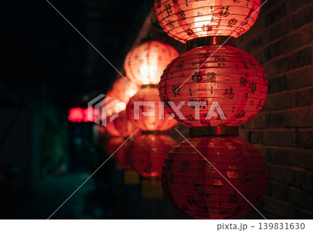 Bright red Chinese lanterns, decorated with gold characters, illuminate a dark brick wall at night Bright red Chinese lanterns, decorated with gold characters, illuminate a dark brick wall at night 139831630