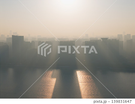 Aerial views of a Chinese cityscape at sunrise show buildings rising above a river. Early morning sun rays shine through the city haze. 139831647