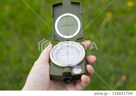 Hand holding open military magnetic compass outdoors on green grass background, navigation equipment for scouting and tourism orientation 139831704