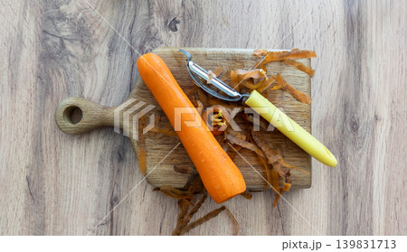 Peeled orange carrot with manual metal peeler tool and fresh shavings on a wooden chopping board culinary vegetable preparation flat lay 139831713