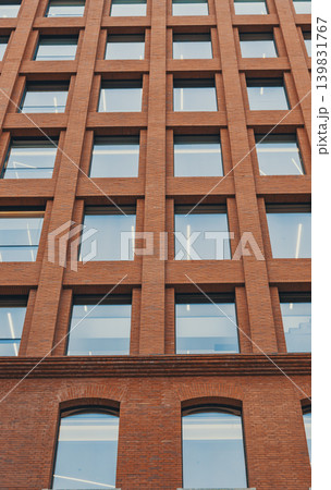 Rising view of a contemporary brick building featuring a grid of many square windows and arched windows on a lower level 139831767