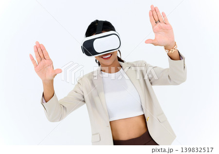 business woman in informal suit wearing VR goggles pointing in the air while standing isolated on white background. concept of Metaverse, virtual reality, future, technology, and internet of things. 139832517