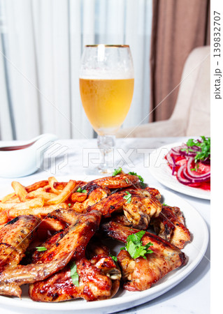 Delicious barbecue chicken wings, with French fries, salad and a refreshing drink, at a cozy table, there are no people Delicious barbecue chicken wings, with French fries, salad and a refreshing drink, at a cozy table, there are no people 139832707