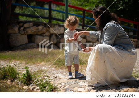 Mother and son enjoying a sunny day at a kids park sharing a tender moment by the water Mother and son enjoying a sunny day at a kids park sharing a tender moment by the water 139832847