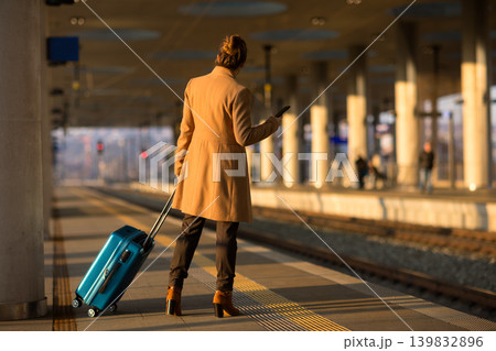 Woman with Teal Suitcase Looking at Phone on Platform Woman with Teal Suitcase Looking at Phone on Platform 139832896