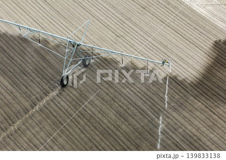 Agricultural irrigation sprinkler watering dry soil on farm field for crops growing during period of drought Agricultural irrigation sprinkler watering dry soil on farm field for crops growing during period of drought 139833138