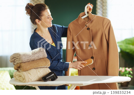 Woman Brushing Camel Coat for Seasonal Wardrobe Care Woman Brushing Camel Coat for Seasonal Wardrobe Care 139833234
