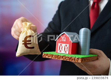 A businessman owns a farm and has a euro in his hands. Buying and selling a farm. Investing in agribusiness. Agricultural assets and rural economy growth. Farmer income, paying taxes. A businessman owns a farm and has a euro in his hands. Buying and selling a farm. Investing in agribusiness. Agricultural assets and rural economy growth. Farmer income, paying taxes. 139833674