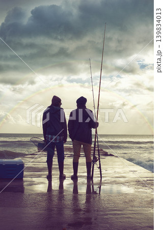 Back, pier and beach with fishermen, sunset or hobby with equipment or weekend break. People, ocean or friends with tools for activity or early morning with waves, shore or seaside with conversation 139834013