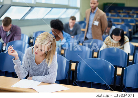 Exam, classroom and student with pen for thinking, assessment and writing at campus. Woman, planning and sitting with paper for brainstorming, education and growth of knowledge in university class 139834071