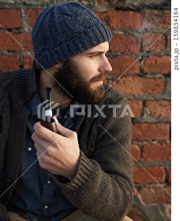 Man, pipe and thinking by brick wall for planning, ideas or smoking in winter with beanie on head. Male person, fashion and tobacco for style, vision or contemplating outdoors on cold morning Man, pipe and thinking by brick wall for planning, ideas or smoking in winter with beanie on head. Male person, fashion and tobacco for style, vision or contemplating outdoors on cold morning 139834164