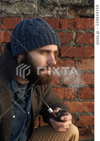 Face, winter and pipe smoke with man outdoor on wall background for fashion, style or clothing. Morning, tobacco or habit and young person with beanie smoking in cold weather season to relax Face, winter and pipe smoke with man outdoor on wall background for fashion, style or clothing. Morning, tobacco or habit and young person with beanie smoking in cold weather season to relax 139834359