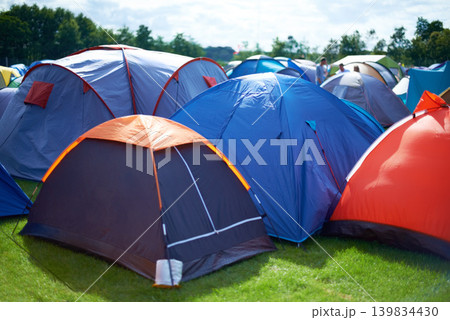 Group, colourful and camping tents in nature outside of a music festival campsite. Row of canopies placed on ground at musical concert, entertainment event and carnival celebration outdoor on grass Group, colourful and camping tents in nature outside of a music festival campsite. Row of canopies placed on ground at musical concert, entertainment event and carnival celebration outdoor on grass 139834430