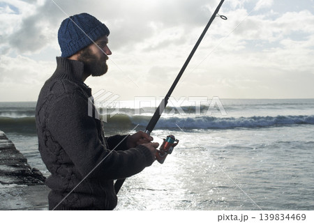 Night, fishing and man at a beach with pole for water hobby, recreation or stress relief vacation in nature. Casting, rod and male fisherman at sea for travel, adventure or fisher sports in Cape Town 139834469