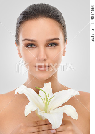 Makeup, floral and portrait of woman in studio with glamour, glow and cosmetic face routine. Beauty, confident and young female person with flower plant for facial cosmetology by gray background. Makeup, floral and portrait of woman in studio with glamour, glow and cosmetic face routine. Beauty, confident and young female person with flower plant for facial cosmetology by gray background. 139834669