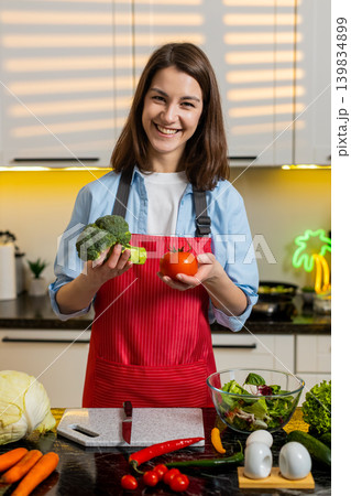 Young woman choosing tomato and broccoli in home kitchen for healthy diet meal prep and nutrition. 139834899