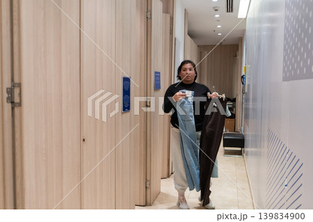 woman holding clothes in fitting room hallway woman holding clothes in fitting room hallway 139834900