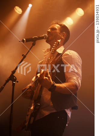 Concert, singer and guitar with man on stage for music, performance and rock show. Event, spotlight and energy with male musician playing instrument at festival club for rave, disco and celebration Concert, singer and guitar with man on stage for music, performance and rock show. Event, spotlight and energy with male musician playing instrument at festival club for rave, disco and celebration 139834931