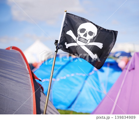 Pirate flag, tent and camping at festival outdoor in summer for party, event or celebration closeup. Skull, crossbones or jolly roger in nature for performance, entertainment or adventure with crowd Pirate flag, tent and camping at festival outdoor in summer for party, event or celebration closeup. Skull, crossbones or jolly roger in nature for performance, entertainment or adventure with crowd 139834989