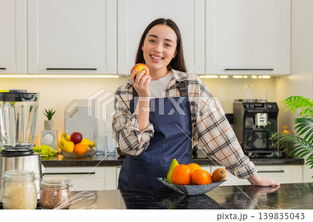 Young woman eating apple in kitchen taking healthy snack break during cooking at home apartment calm Young woman eating apple in kitchen taking healthy snack break during cooking at home apartment calm 139835043