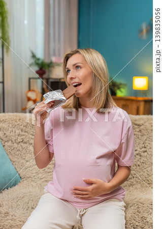 Pregnant woman tasting dark chocolate rolling eyes in delight rubbing belly enjoying sweet pleasure 139835056