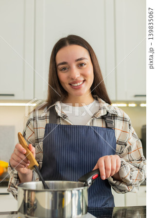 Young woman stirring hot vegetable soup in kitchen pot preparing healthy homemade lunch meal at home Young woman stirring hot vegetable soup in kitchen pot preparing healthy homemade lunch meal at home 139835067